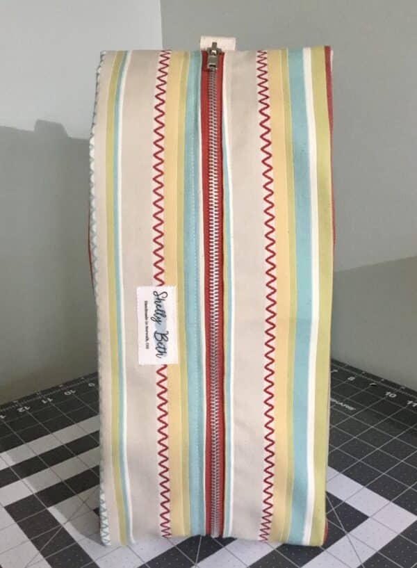 Closed wine bag with 2 bottles stored. Multi-colored material with red metal zipper and handle.