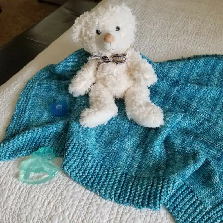Sample of Beechtree Baby Blanket Knitting Pattern knit with turquoise yarn with a white Teddy bear sitting on the blanket.
