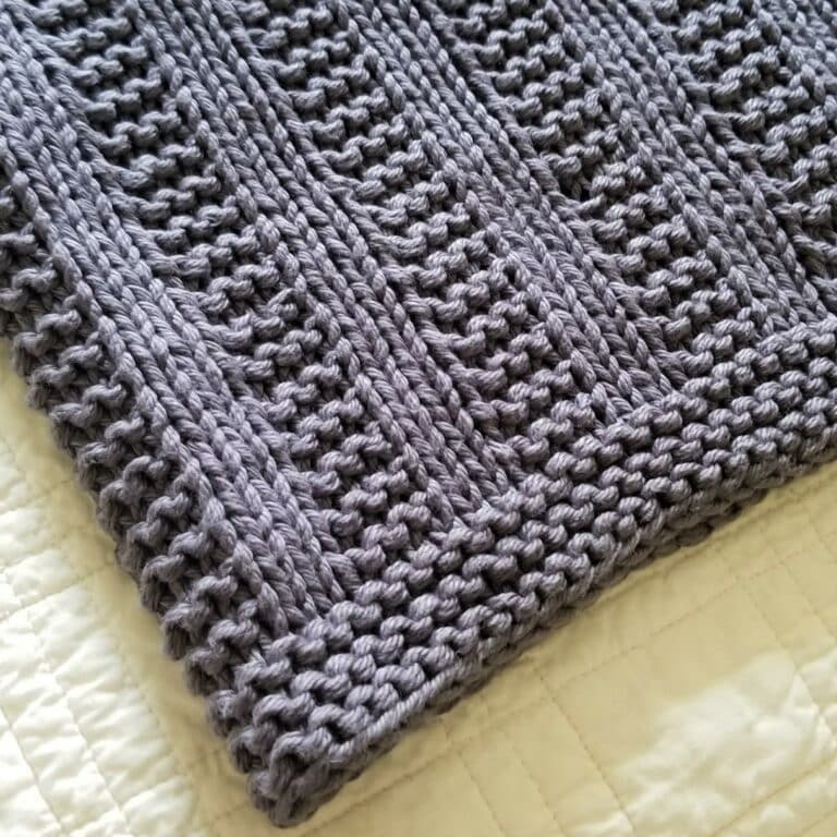 Sample of Darby baby blanket knitted in gray yarn with a white teddy bear