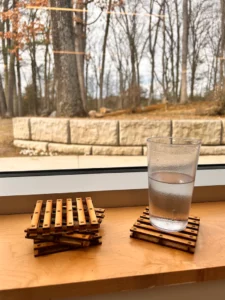 A Picture of a cup on top of a pallet coaster. 2 Pallet coaster sit stacked next to it.
