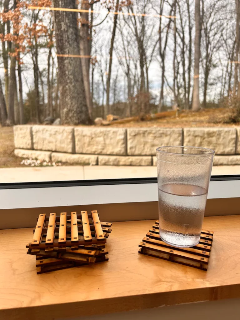 A Picture of a cup on top of a pallet coaster. 2 Pallet coaster sit stacked next to it.