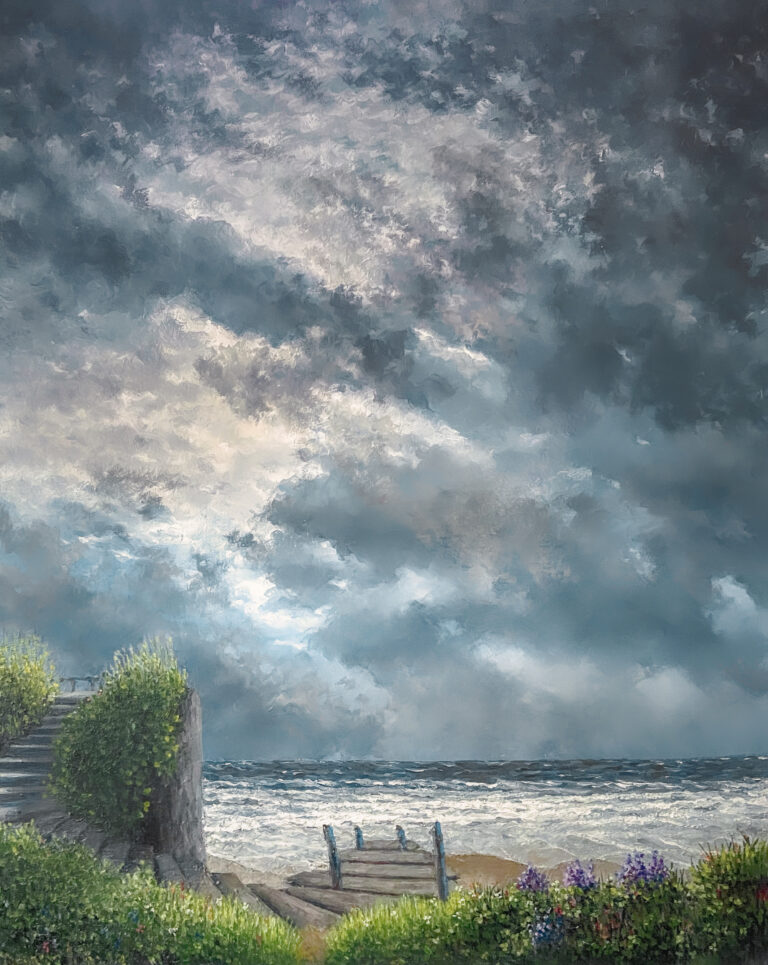 Seascape with deck stairs surrounded by boulders. On the right side of the steps leading to the beach is a small grassy cliff. The beach has choppy surf. There is a dark sky with flowing clouds.