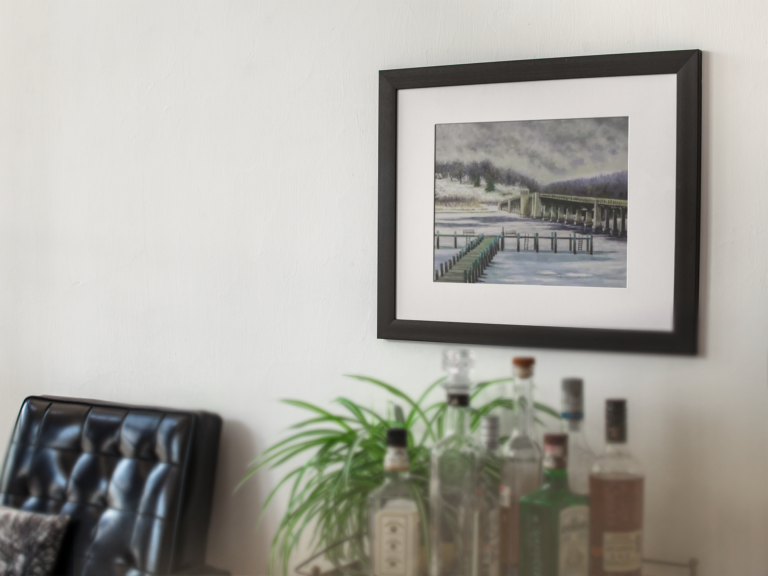 template of a framed art print on a white wall with a black armchair and bottles nearby a14689 Rumson Bridge