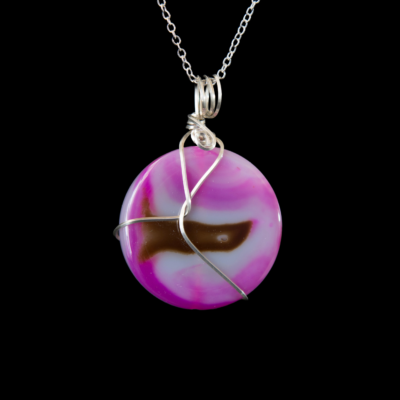 Brazilian Agate Pendant. Disc shaped pink, white and brown stone with a square Sterling Silver abstract wire wrap. This pendant The pendant hangs from a silver chain and is on a black background.