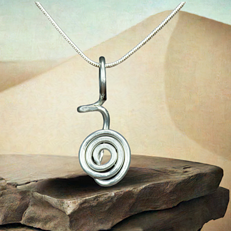 Cho Ku Rei silver colored reiki pendant on a stone with sand in the background.