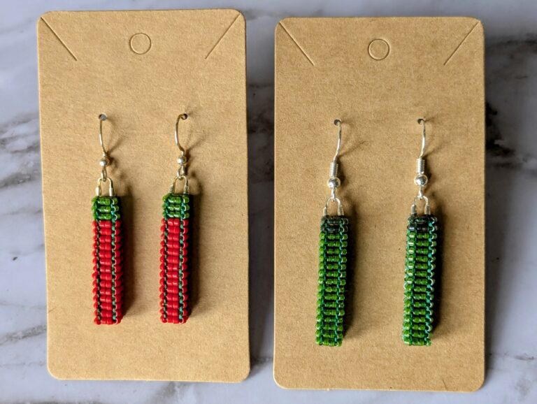 Two pairs of festive cubic pillar (skinny squared rectangles) beaded earrings displayed side by side on brown earring cards. The pair on the left is red while the one on the right is green.