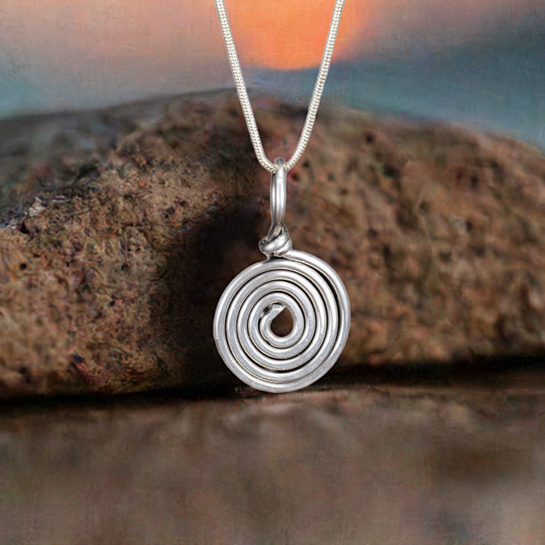 Hammered aluminum silver swirl pendant with a rock in the background.