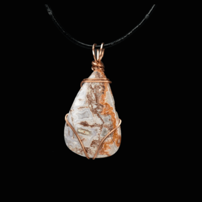 Brown and white teardrop stone minimally wrapped in copper wire. The pendant is shown on a black leather cord and is pictured on a black background.