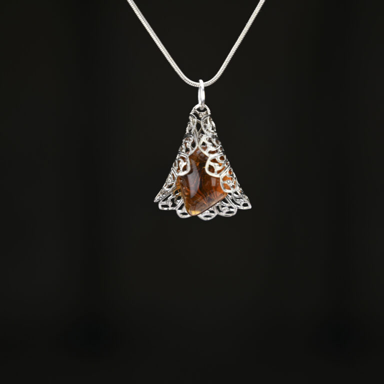 Tumbled amber stone wrapped in silver colored filigree wrap. The pendant hangs on a silver snake chain.