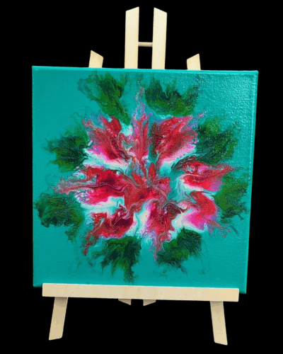 A 10x10 fluid art painting displayed on a wooden easel: the composition is floral with the bloom being shades of red, pink, and white. The leaves are medium and darker shades of green, and the background is bright turquoise.