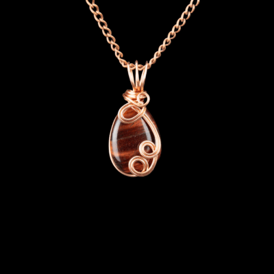 Brown tigers eye teardrop shaped pendant. The stone is wrapped in copper wire with 3 decorative swirls and a 3 hoop bail. It is shown on a copper chain.