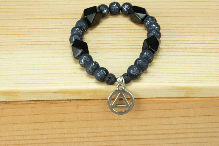 Onyx and black fire agate bracelet with a silver recovery charm. Charm is a circle with a triangle in the center which traditionally represents recovery from alcohol addiction.