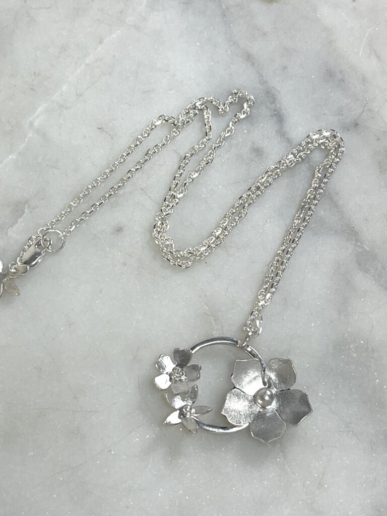 flat lay of sterling silver flower wreath pendant necklace