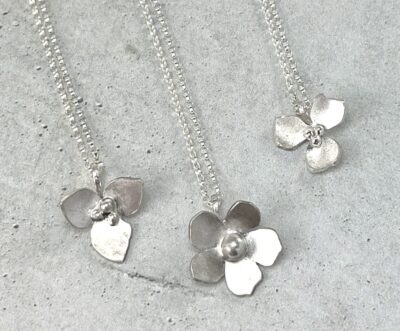 three sterling silver flower pendant necklaces flat on a gray background