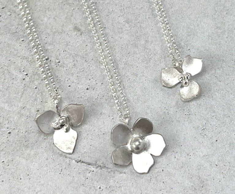 three sterling silver flower pendant necklaces flat on a gray background