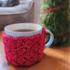 Mug of tea with a red crochet cozy on it, sitting on a table.