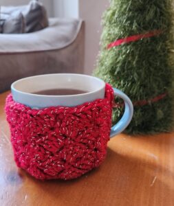 Mug of tea with a red crochet cozy on it, sitting on a table.