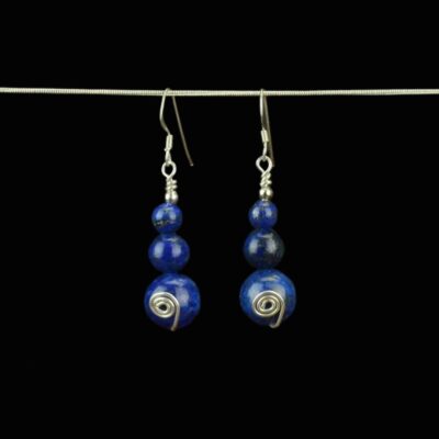 Deep blue lapis lazuli earrings created with three beads. The bottom bead is 12mm the middle bead is 8mm and the top lapis bead is 6mm. There is a handcrafted sterling silver swirl on each of the 12mm beads. The earrings have sterling silver French ear wires and they are hanging from a chain for display.