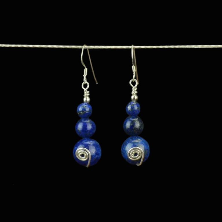 Deep blue lapis lazuli earrings created with three beads. The bottom bead is 12mm the middle bead is 8mm and the top lapis bead is 6mm. There is a handcrafted sterling silver swirl on each of the 12mm beads. The earrings have sterling silver French ear wires and they are hanging from a chain for display.