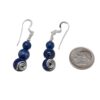 Blue lapis lazuli bead earrings with a silver swirl on each of the larger beads. They are laying on a white background next to a dime for size comparison.