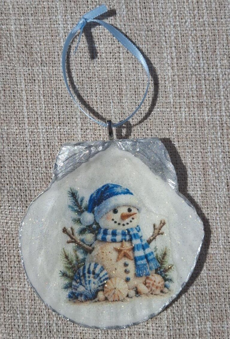 Handmade Coastal Christmas Snowman Seashell Ornament – Blue Winter Beach Decor 1 Handmade coastal snowman ornament on a scallop seashell with blue winter artwork and a light-blue ribbon hanger