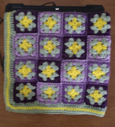 A lovingly handcrafted crochet baby lapghan blanket in enchanting shades of purple and green